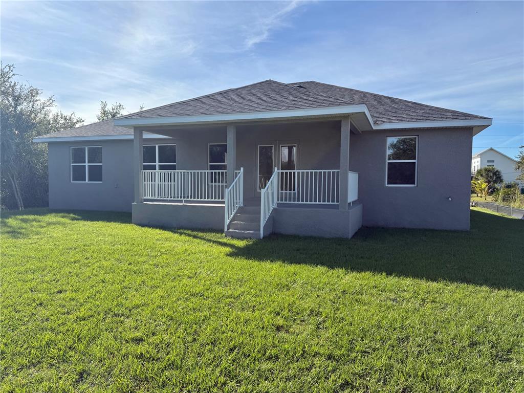 The rear exterior of a gray house features a covered porch with white railings — 9527 IMPALA CIRCLE, PORT CHARLOTTE, FL