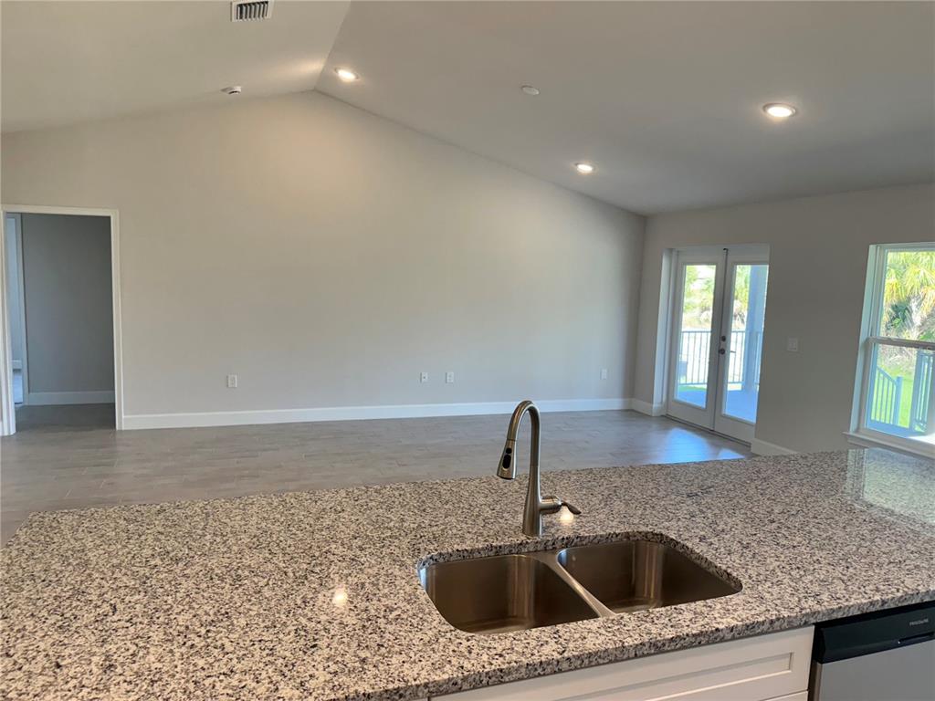 A kitchen island with a granite countertop and stainless steel sink overlooks an open living area — 9527 IMPALA CIRCLE, PORT CHARLOTTE, FL
