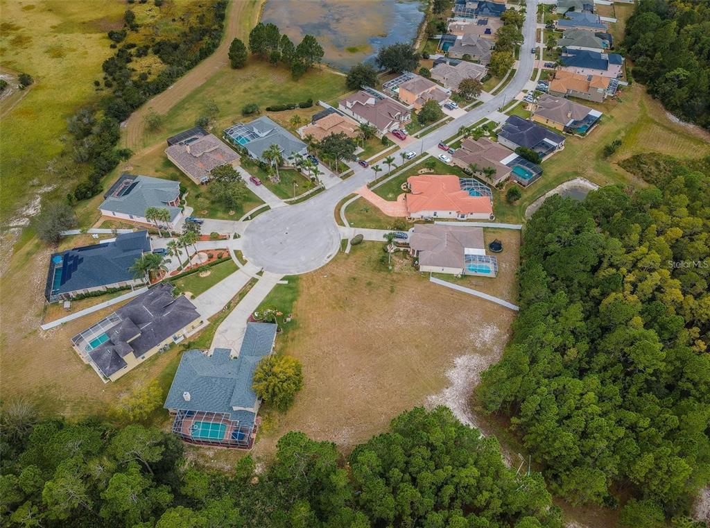 An aerial view shows a suburban cul-de-sac with several houses, swimming pools, and surrounding woods — 00 SHOOTING STAR COURT, NEW PORT RICHEY, FL