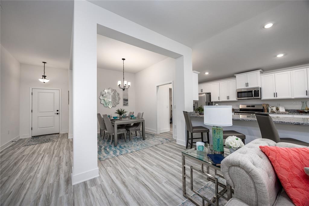An open-concept living area features a dining room, kitchen with white cabinets, and wood-look flooring — 13622 NW 150TH CIRCLE, ALACHUA, FL