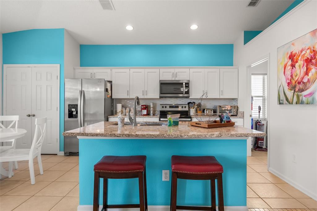 A kitchen features a granite-topped island, white cabinetry, and bright blue accent walls — 2254 WYNDHAM PALMS WAY, KISSIMMEE, FL