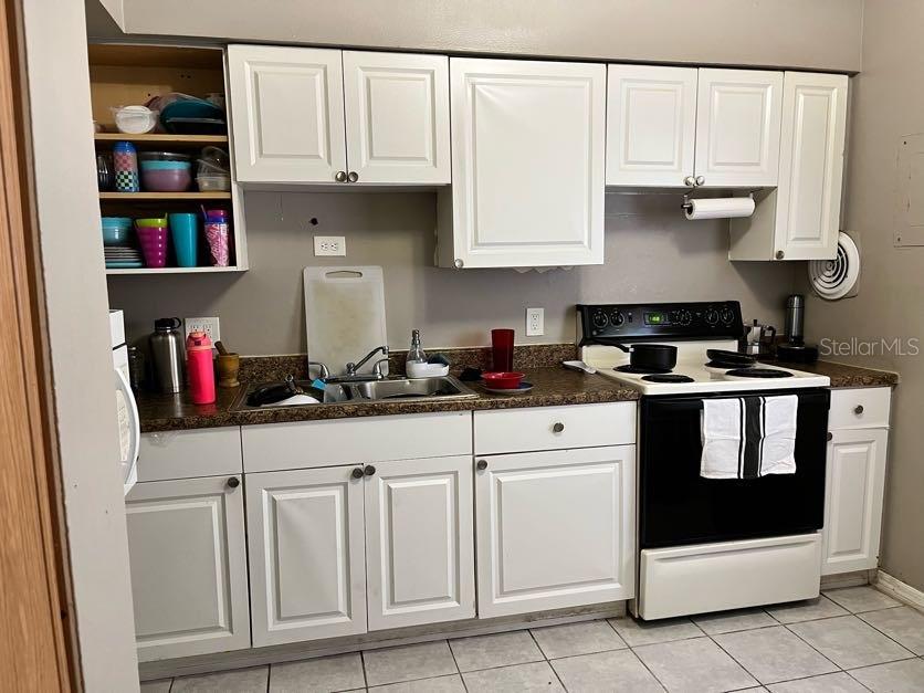 A kitchen features white cabinets, a dark countertop, a stainless steel sink, and a white stove — 5885 DAHLIA DRIVE UNIT 31/116, ORLANDO, FL