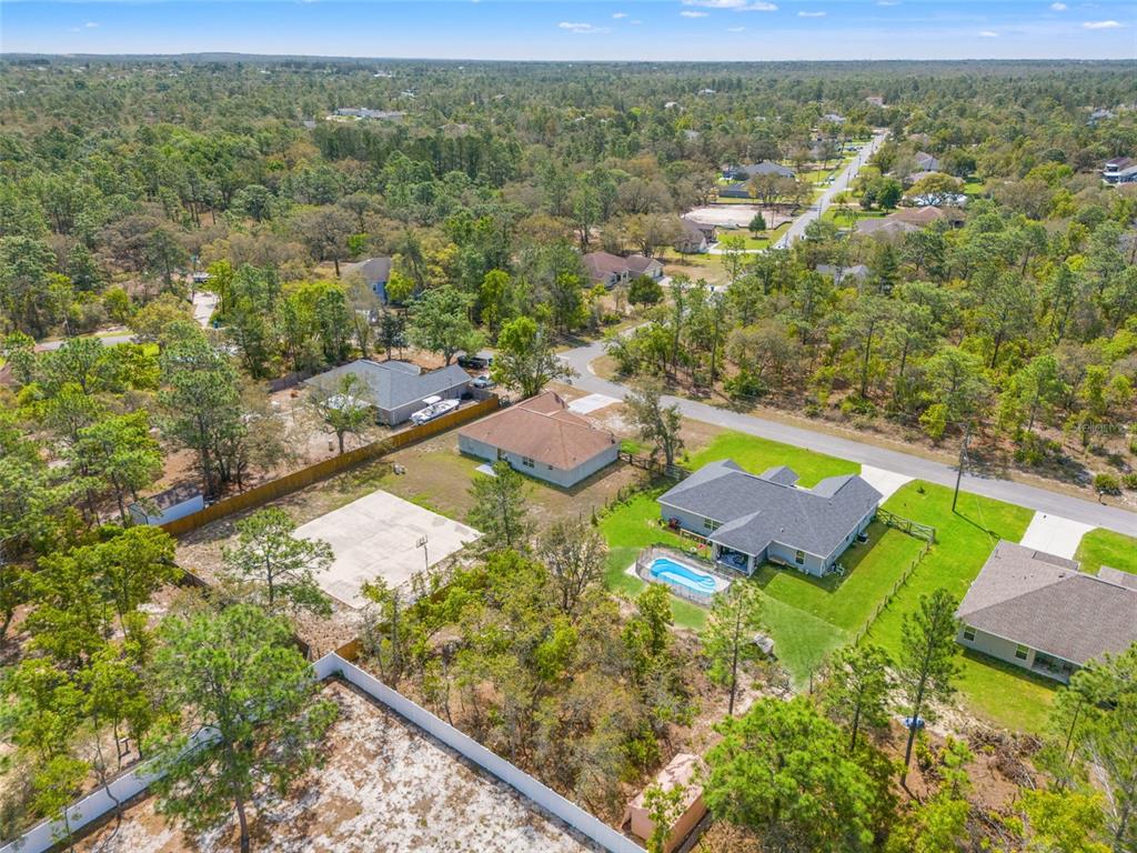 An aerial view shows several suburban houses with pools and yards surrounded by dense trees — 12015 PHOENIX AVENUE, WEEKI WACHEE, FL