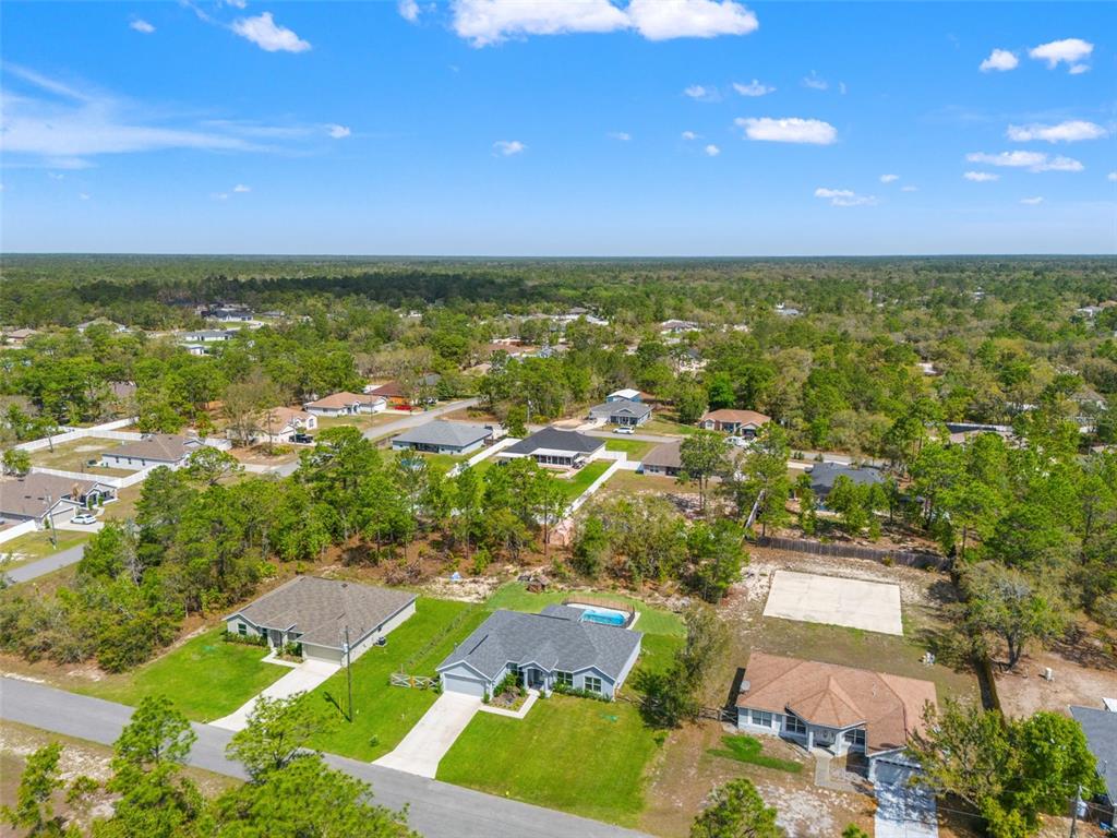 An aerial view shows several single-family homes surrounded by trees and a clear blue sky — 12015 PHOENIX AVENUE, WEEKI WACHEE, FL