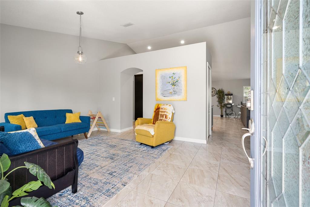 A living room with tile flooring, a blue sofa, a yellow armchair, and vaulted ceilings — 12015 PHOENIX AVENUE, WEEKI WACHEE, FL