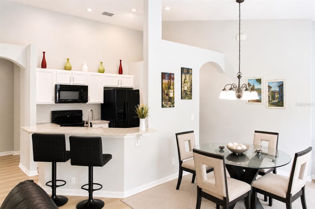 A kitchen with white cabinets and black appliances opens to a dining area with seating — 2520 DHARMA CIRCLE, KISSIMMEE, FL
