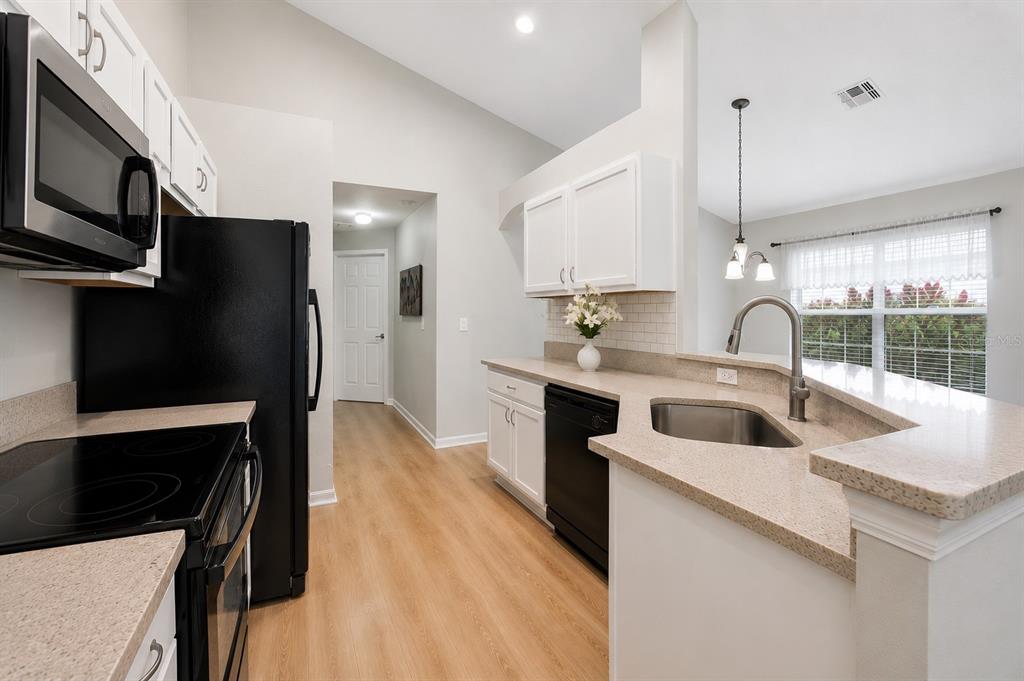 A kitchen with white cabinets, black appliances, light countertops, and wood-look flooring — 2520 DHARMA CIRCLE, KISSIMMEE, FL