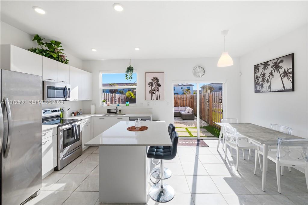 A modern kitchen features white cabinetry, a central island with bar stools, and a dining area — 12245 NW 24th Pl, Miami FL 33167, MIAMI, FL
