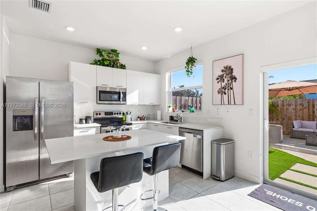 A modern kitchen features white cabinetry, stainless steel appliances, a quartz island, and patio access — 12245 NW 24th Pl, Miami FL 33167, MIAMI, FL
