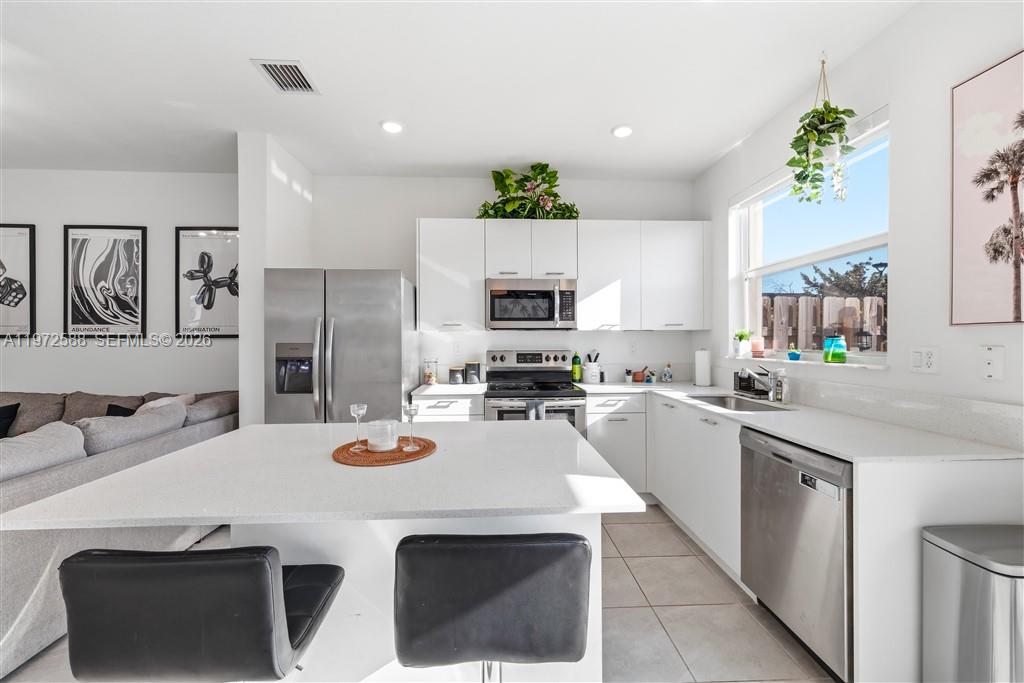 A modern kitchen features white cabinetry, stainless steel appliances, a central island, and tile flooring — 12245 NW 24th Pl, Miami FL 33167, MIAMI, FL