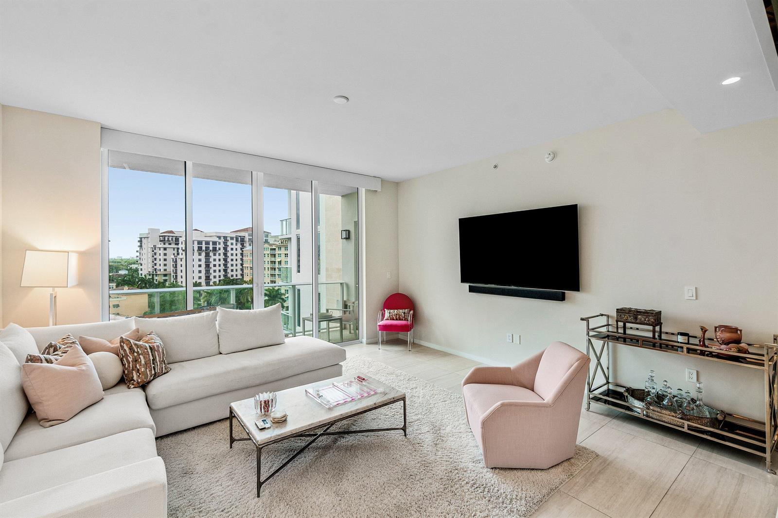 A modern living room features a white sectional sofa, pink armchair, and floor-to-ceiling windows — 200 SE Mizner Boulevard # 810, Boca Raton FL 33432, BOCA RATON, FL