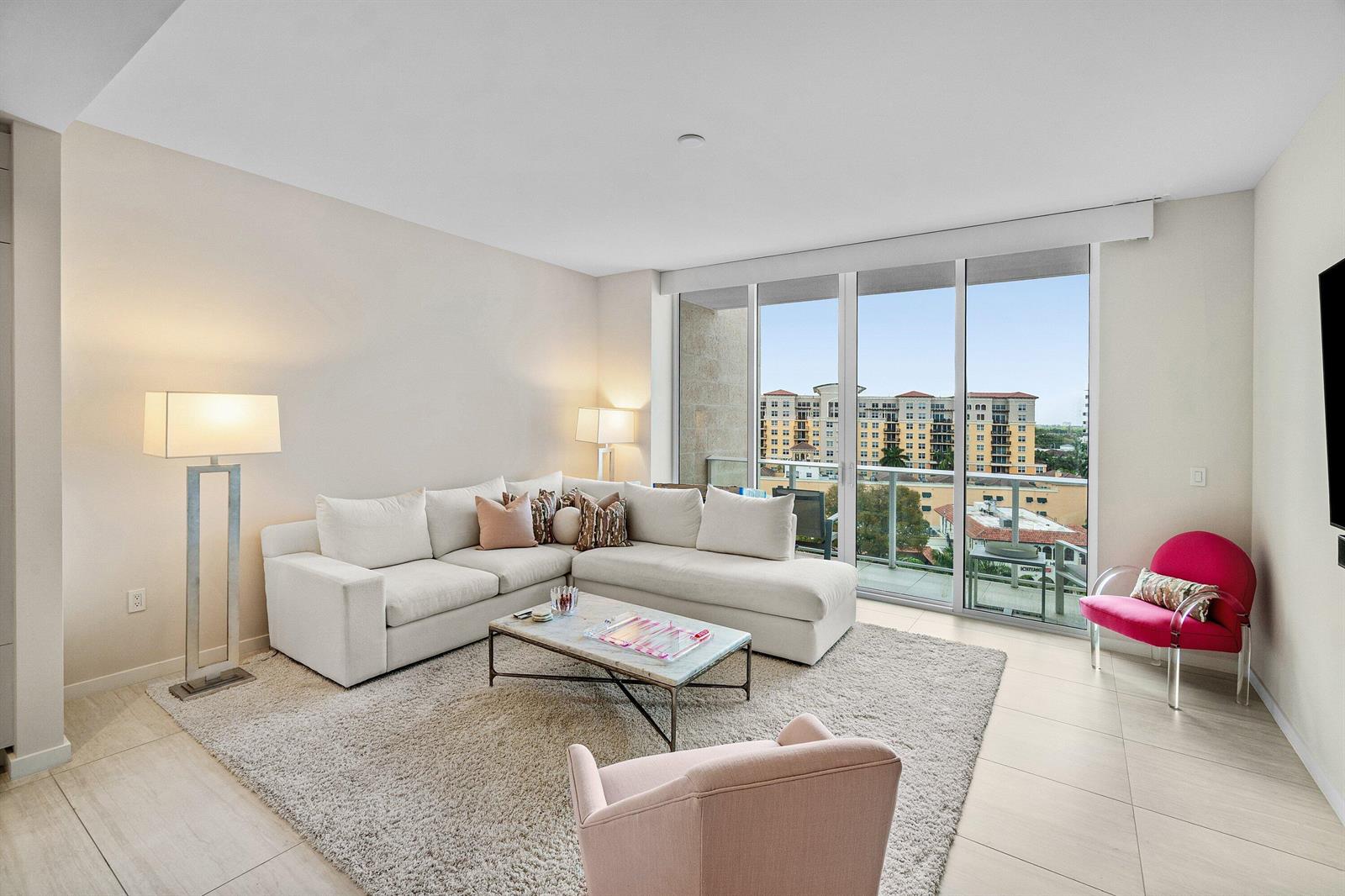 A modern living room features a white sectional sofa, a coffee table, and balcony views — 200 SE Mizner Boulevard # 810, Boca Raton FL 33432, BOCA RATON, FL