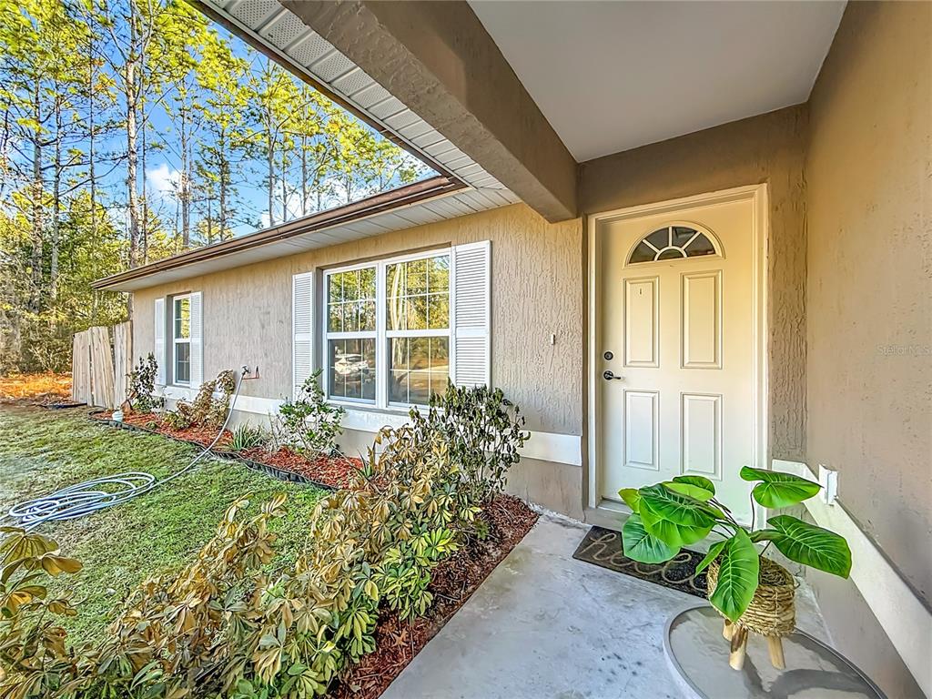A tan house exterior features a front door, a window with shutters, and landscaping — 14321 SW 79TH TERRACE, OCALA, FL