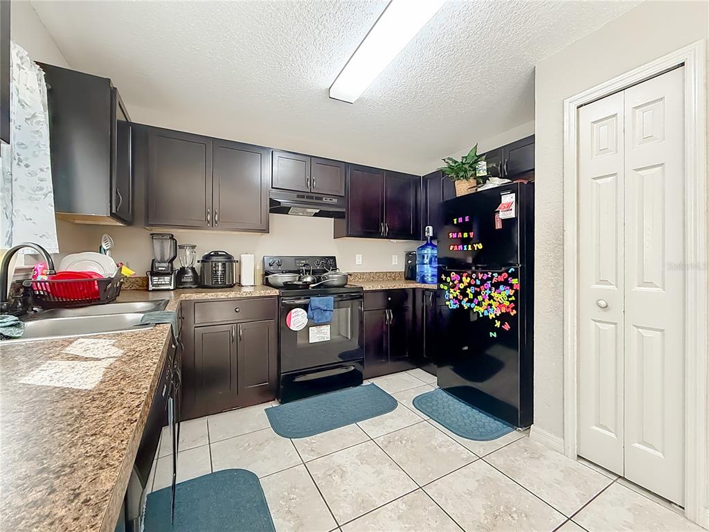 A kitchen features dark wood cabinets, black appliances, granite countertops, and light-colored tile flooring — 14321 SW 79TH TERRACE, OCALA, FL