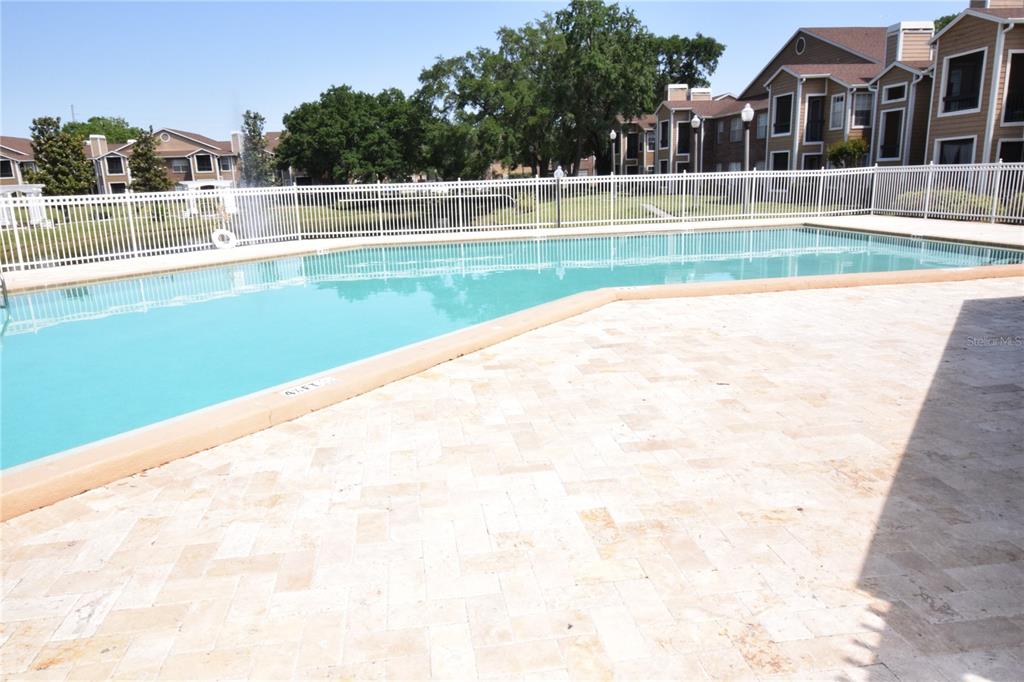 A swimming pool with a light-colored paver deck is enclosed by a white metal fence — 5533 CHRISHIRE WAY UNIT F201, ORLANDO, FL