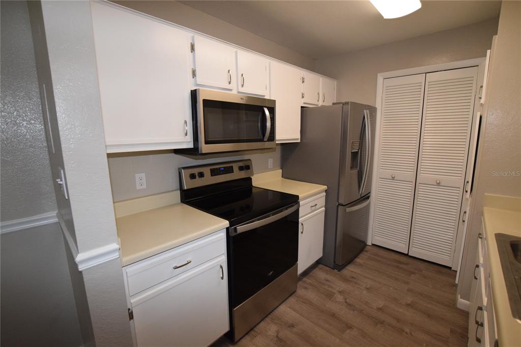 A kitchen with white cabinets, stainless steel appliances, and wood-look flooring — 5533 CHRISHIRE WAY UNIT F201, ORLANDO, FL