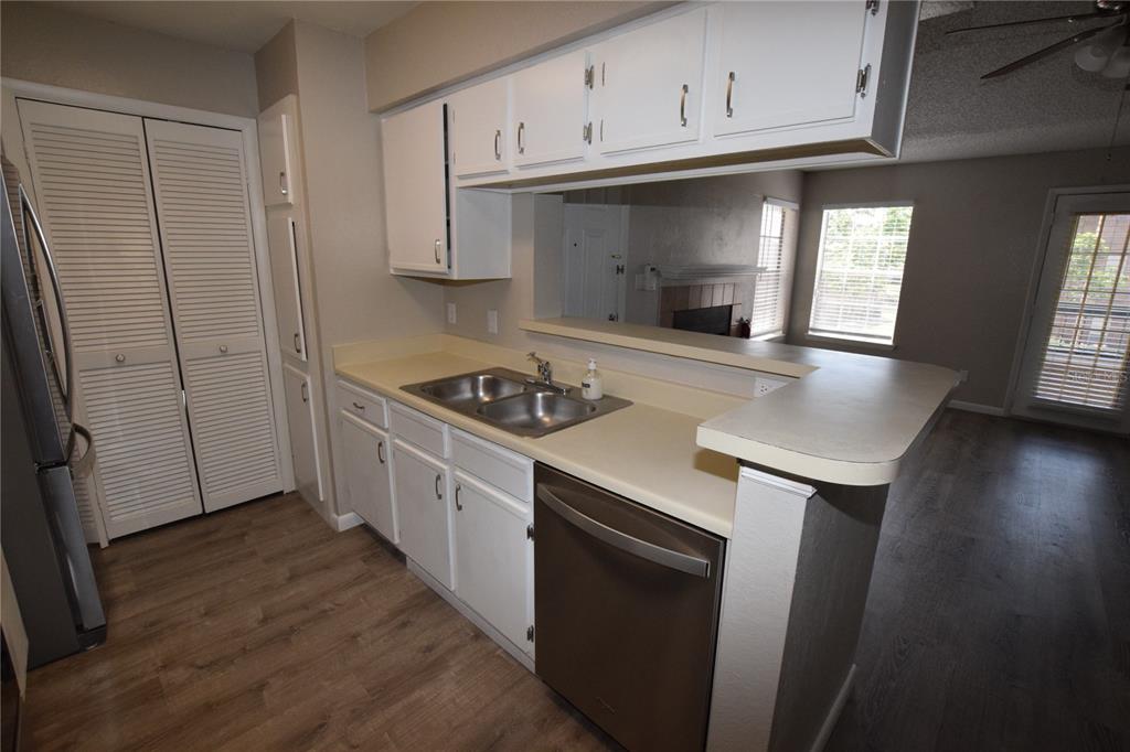 A kitchen with white cabinets, laminate countertops, a stainless steel dishwasher, and wood-look flooring — 5533 CHRISHIRE WAY UNIT F201, ORLANDO, FL