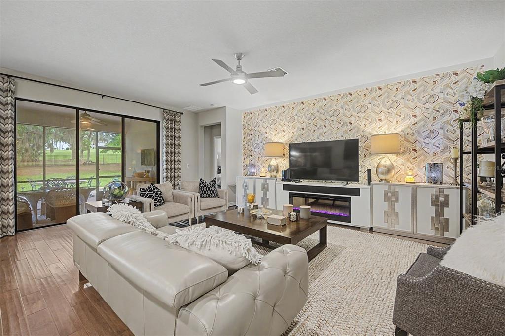 A living room features a tufted sofa, patterned wallpaper, a fireplace, and sliding glass doors — 4926 SOUTHERN VALLEY LOOP, BROOKSVILLE, FL