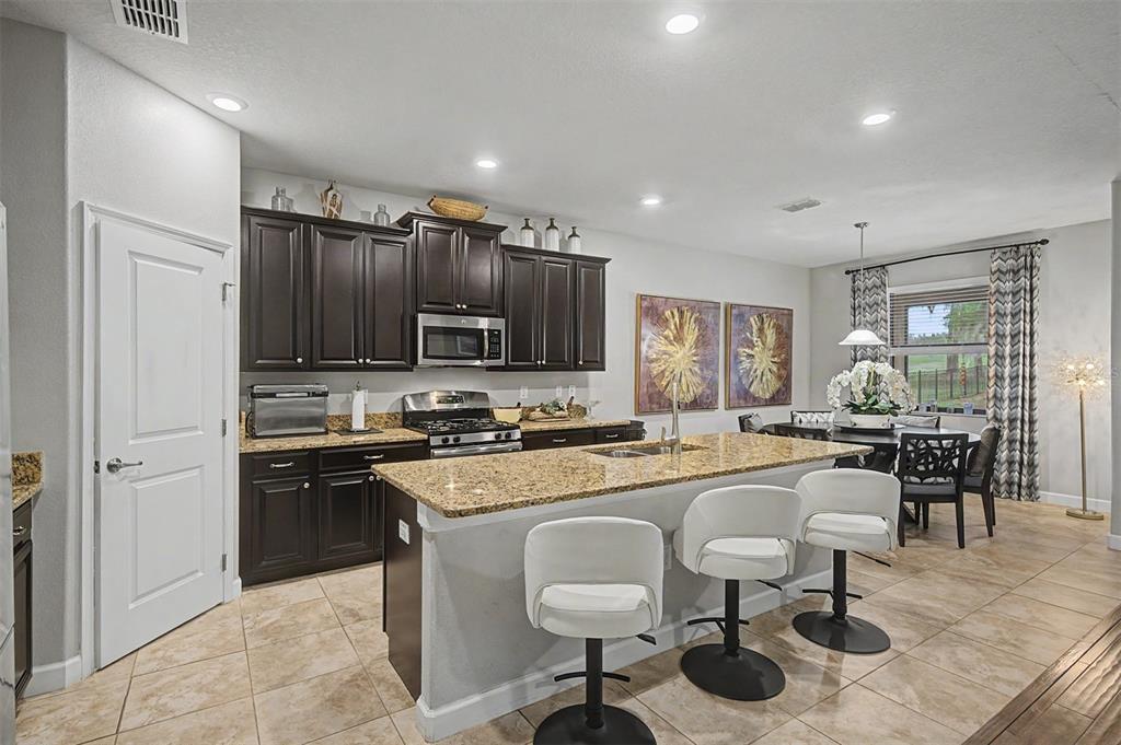 A kitchen features dark wood cabinets, granite countertops, a central island, and white bar stools — 4926 SOUTHERN VALLEY LOOP, BROOKSVILLE, FL