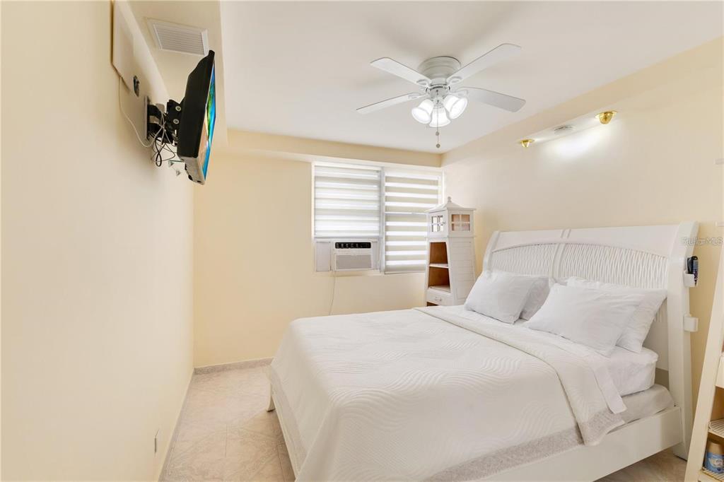 A bedroom features a white bed, a ceiling fan, and a wall-mounted television — 5890 JOSE M TARTAK AVE UNIT 704A, CAROLINA, PR