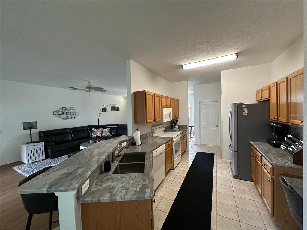 A kitchen with wood cabinets and gray countertops overlooks a living room with a sofa — 24308 WESTGATE BOULEVARD, PUNTA GORDA, FL