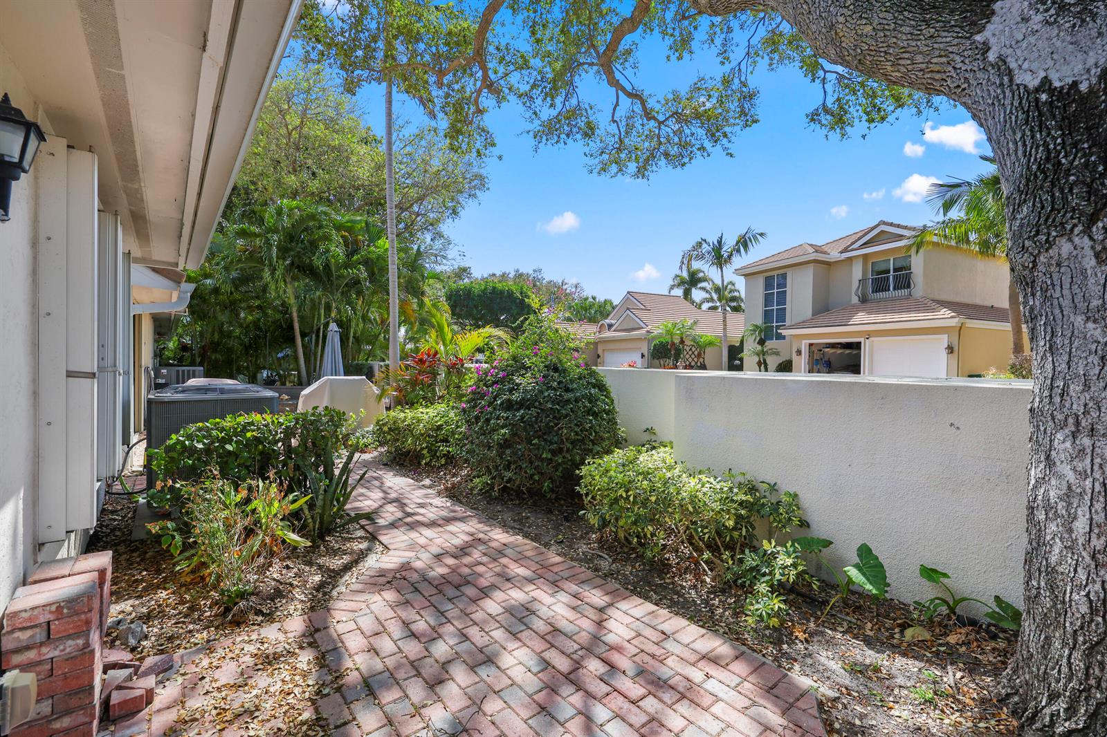 A brick walkway leads through a landscaped side yard past a house and privacy wall — 461 Coral Cove Drive, Juno Beach FL 33408, JUNO BEACH, FL
