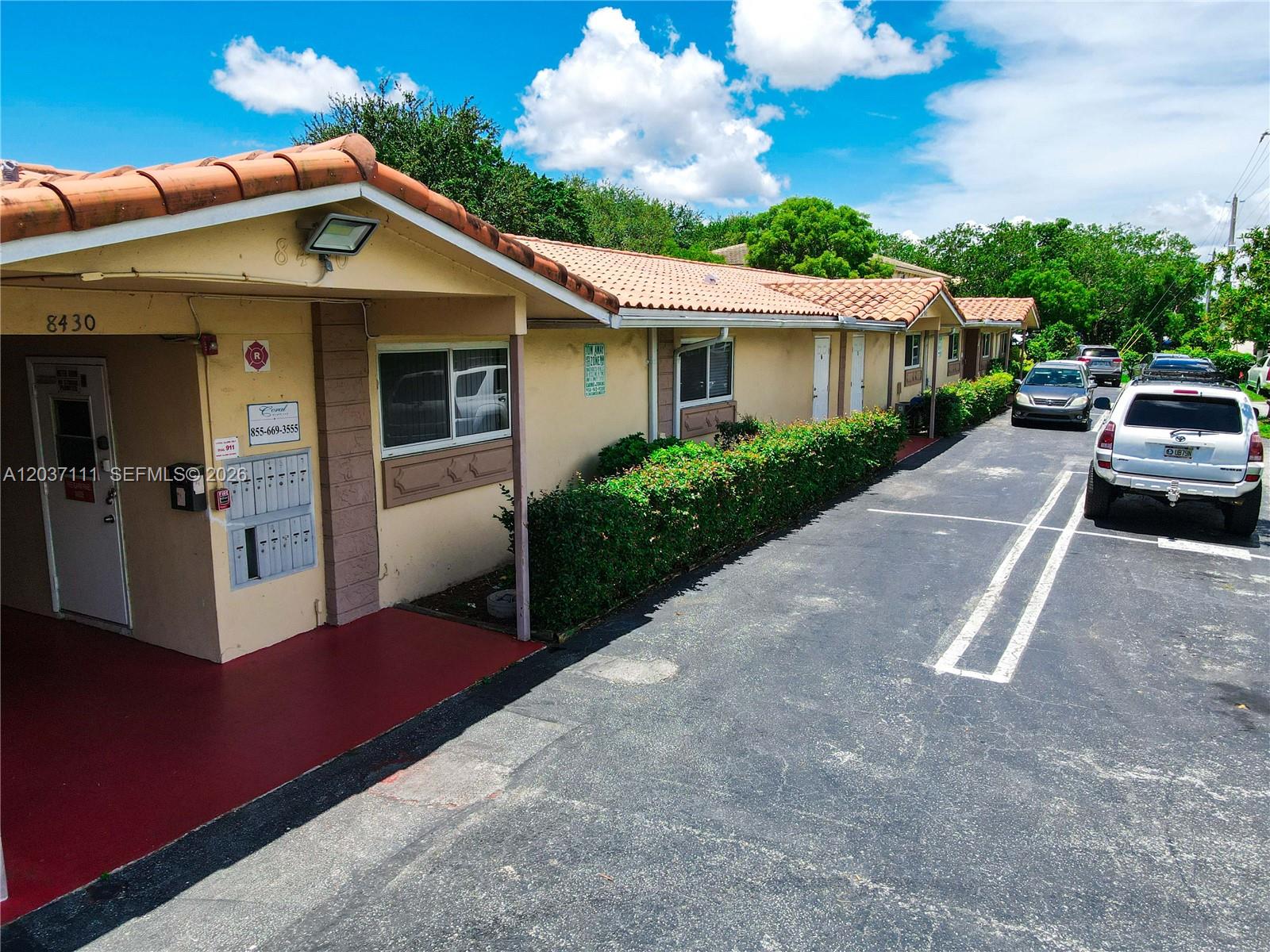 An exterior view of a single-story apartment building with a parking lot and landscaping — CORAL SPRINGS, FL