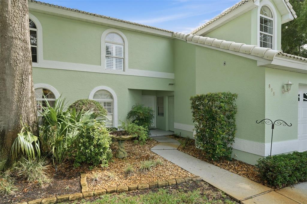 A two-story house with light green stucco walls, arched windows, and a concrete walkway — 808 LANARK COURT, INVERNESS, FL