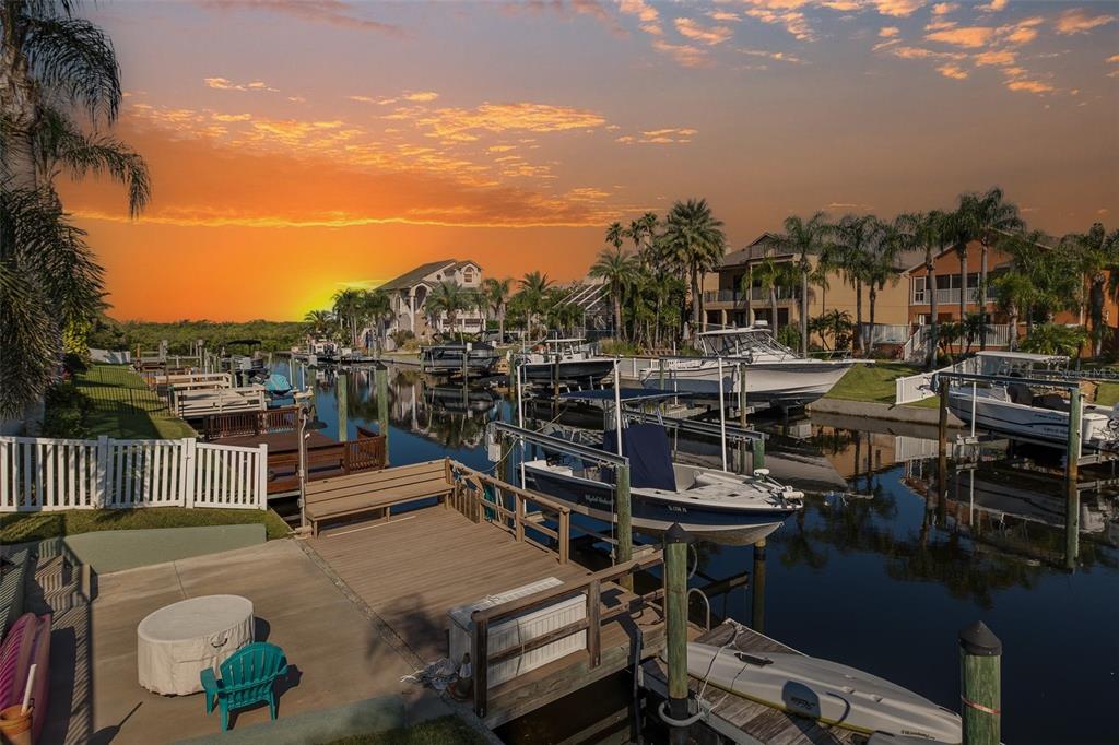 A residential dock with a boat lift and parked boats overlooks a canal at sunset — 4335 SANDDOLLAR COURT, NEW PORT RICHEY, FL