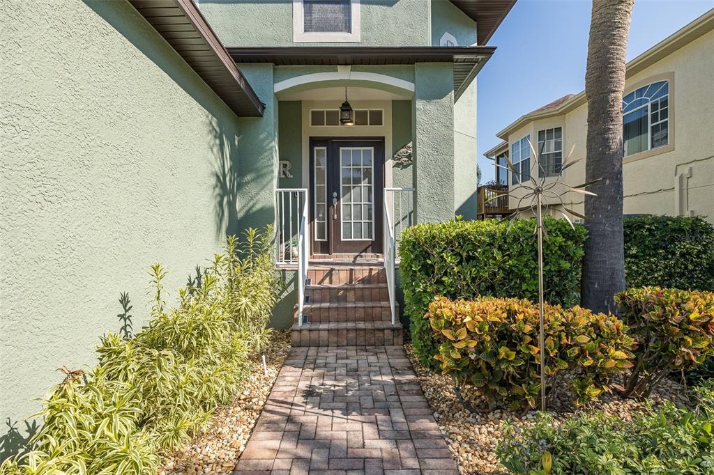 A paved walkway leads to the front entrance of a green house with a palm tree — 4335 SANDDOLLAR COURT, NEW PORT RICHEY, FL