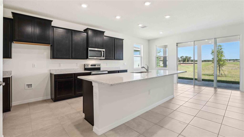 A kitchen features dark cabinets, granite countertops, a center island, and sliding glass patio doors — 8172 IVES PLACE, WILDWOOD, FL