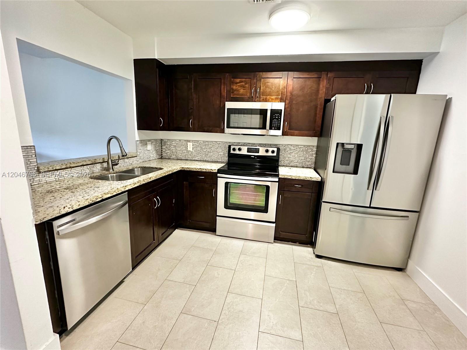 A kitchen features dark wood cabinets, granite countertops, stainless steel appliances, and light tile flooring — 4245 S Pine Island Rd, Davie FL 33328, DAVIE, FL