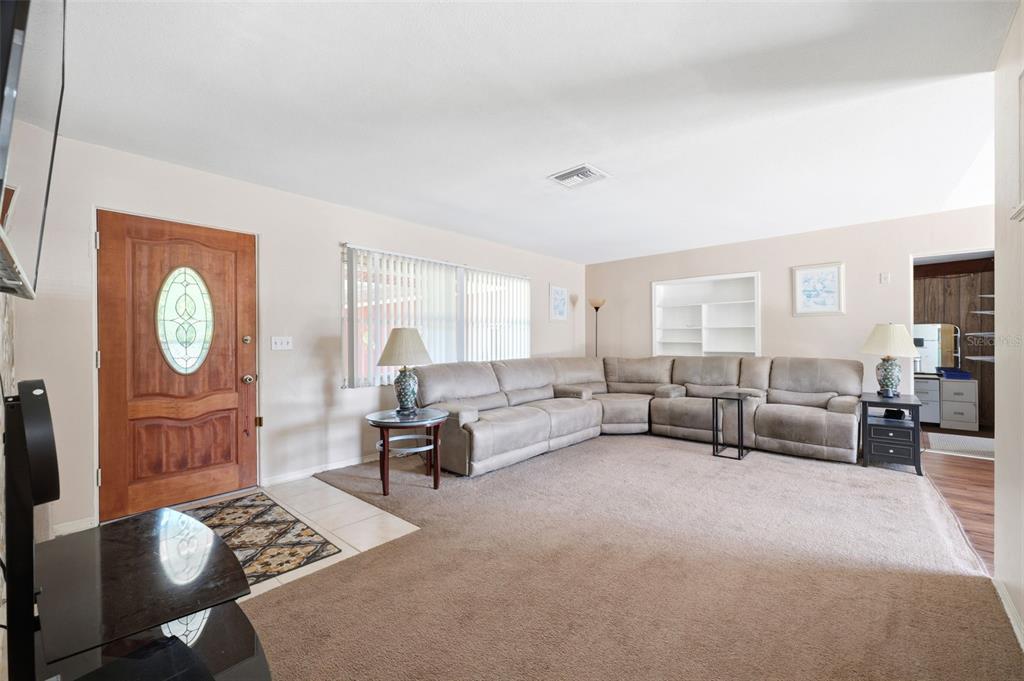 A living room features a large sectional sofa, beige carpeting, and a wooden front door — 764 NE 13TH STREET, CRYSTAL RIVER, FL