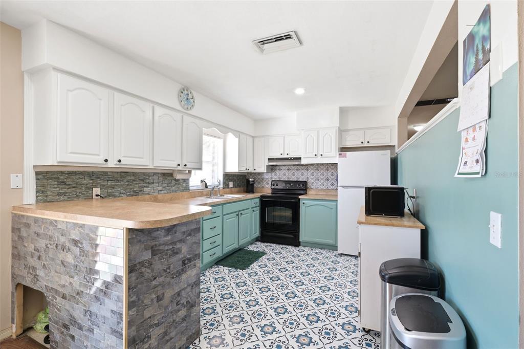 A kitchen features white upper cabinets, teal lower cabinets, patterned floor tiles, and stone-tiled counters — 764 NE 13TH STREET, CRYSTAL RIVER, FL