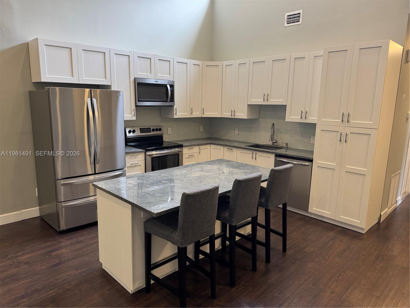 A modern kitchen features white cabinetry, stainless steel appliances, a gray island, and dark flooring — 20478 Via Marisa, Boca Raton FL 33498, BOCA RATON, FL