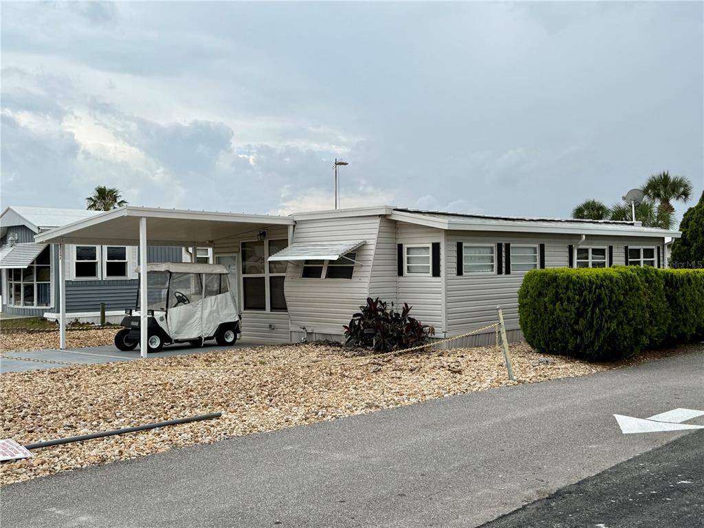 A light-colored mobile home features a covered carport with a golf cart parked underneath — 317 GOLF CREST LANE UNIT 58, DAVENPORT, FL