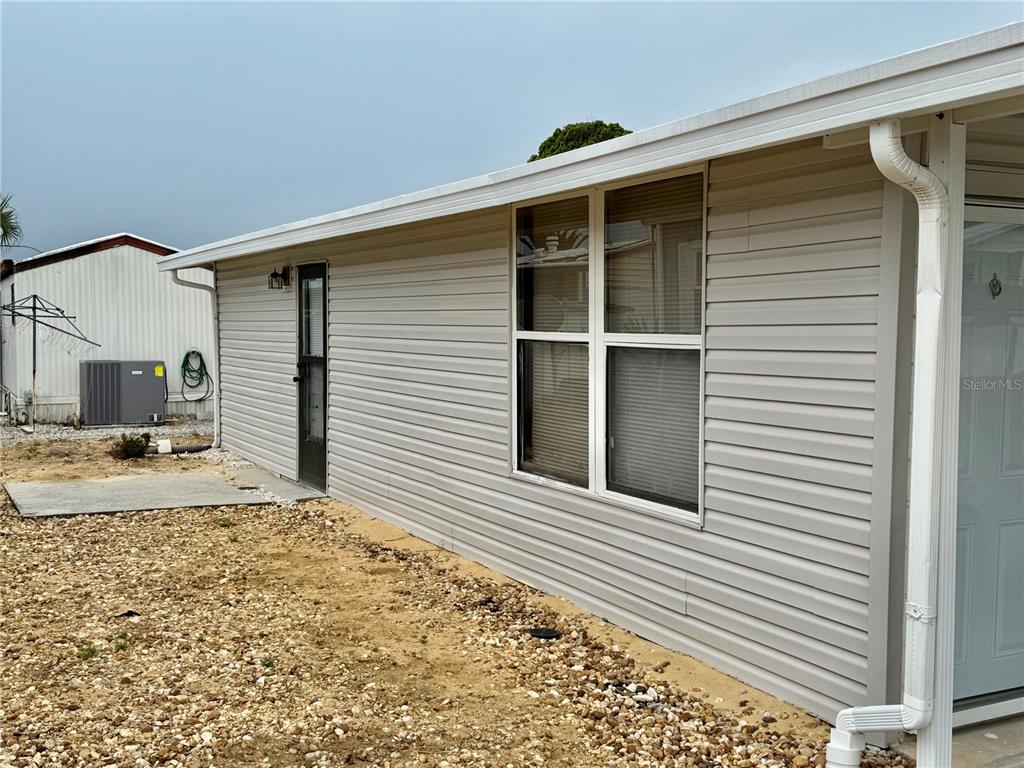 The exterior side of a light-colored mobile home features vinyl siding and a gravel yard — 317 GOLF CREST LANE UNIT 58, DAVENPORT, FL