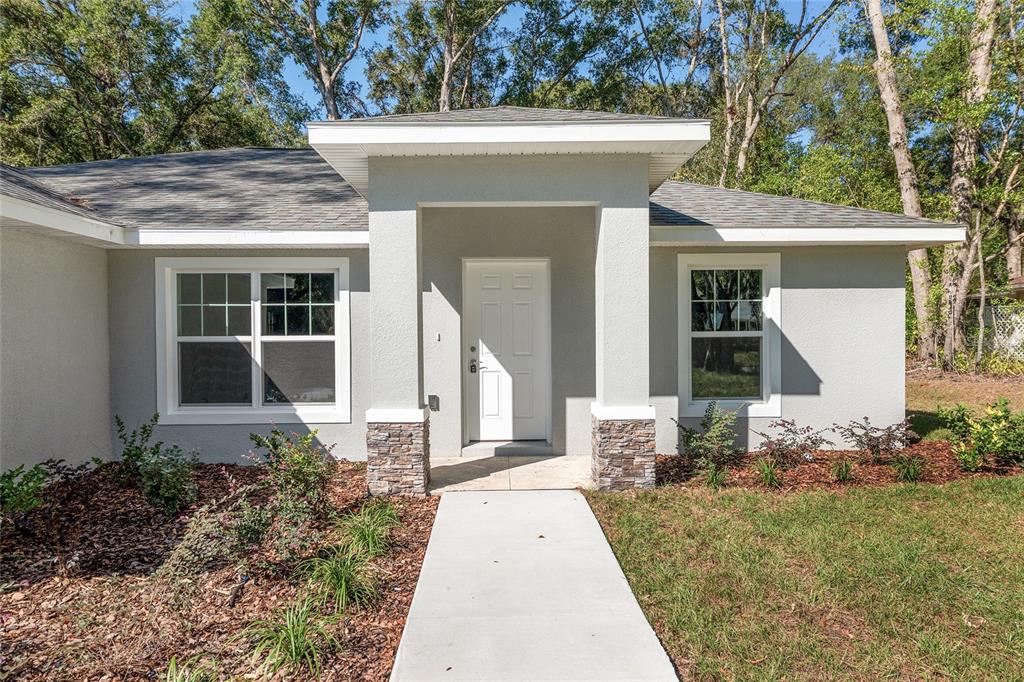The exterior of a single-story house features a covered entryway with stone-accented pillars — 10070 SW 192ND CIRCLE, DUNNELLON, FL