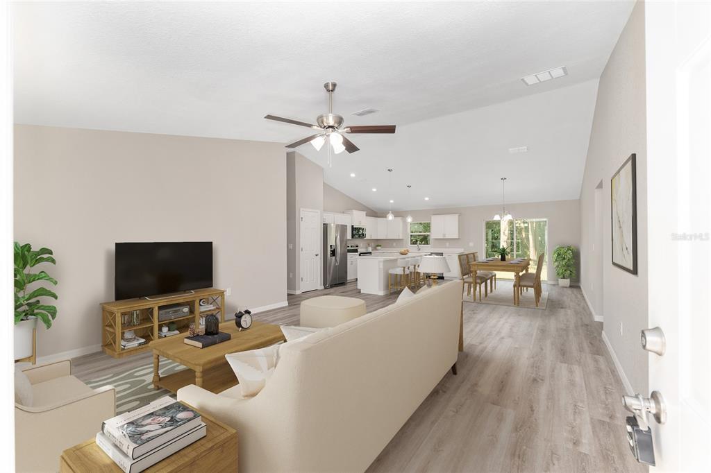 A bright open-concept living room and kitchen feature vaulted ceilings and light wood-look flooring — 10070 SW 192ND CIRCLE, DUNNELLON, FL