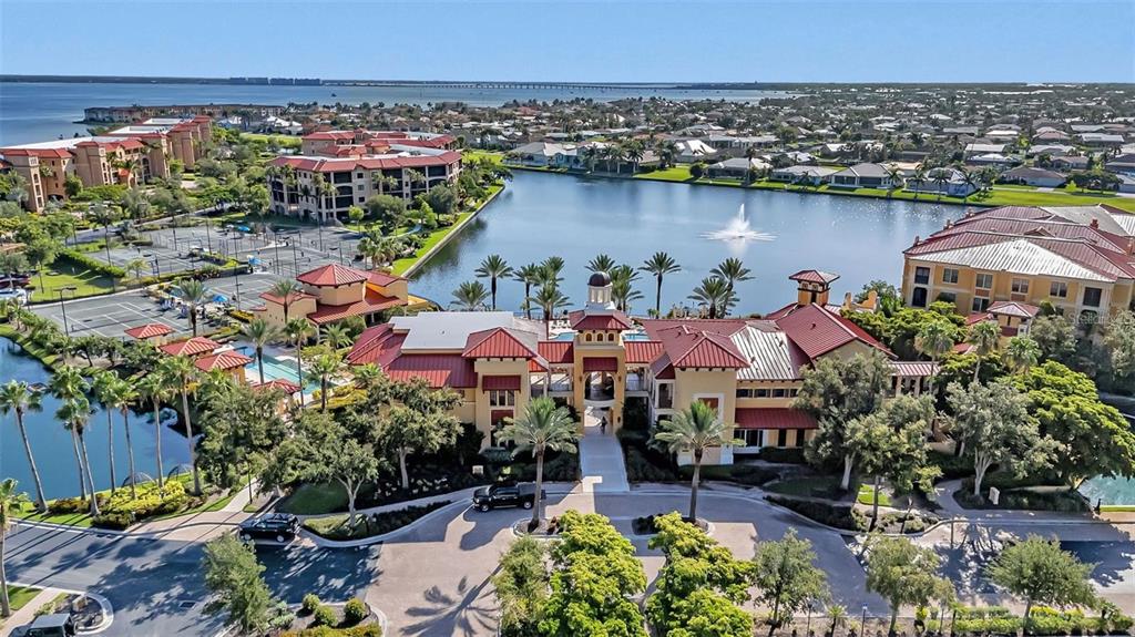 An aerial view shows a large Mediterranean-style clubhouse complex with a pool and lake — 99 VIVANTE BOULEVARD UNIT 9949, PUNTA GORDA, FL