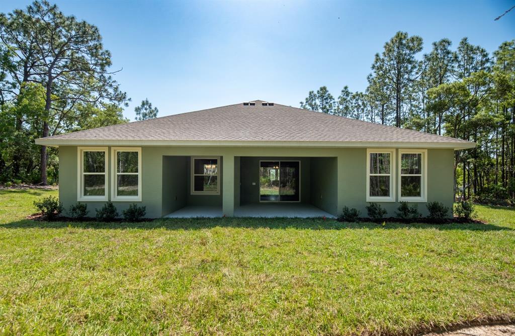 The rear exterior of a single-story house features a covered patio and a grassy yard — 13454 SW 67TH LANE, OCALA, FL