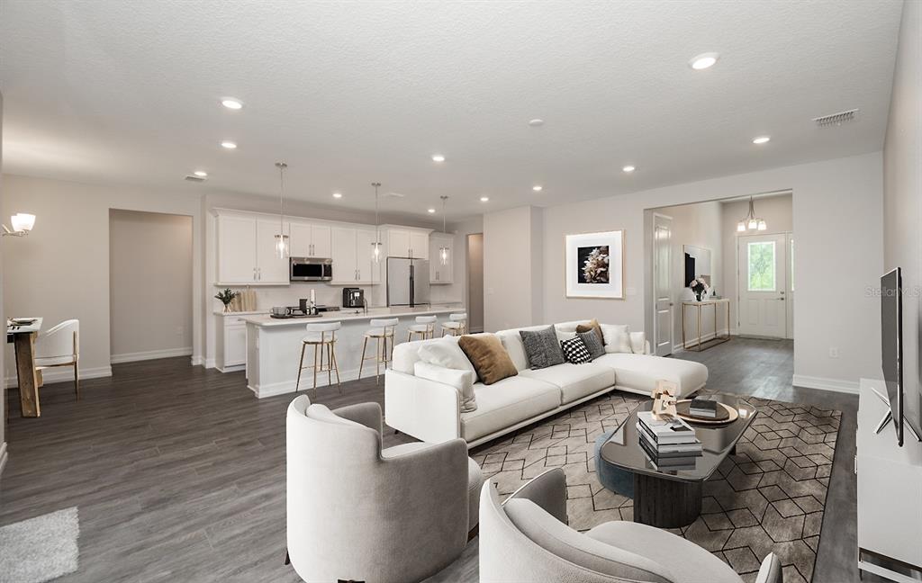 An open-concept living room and kitchen featuring white cabinetry, a large sectional, and wood flooring — 13454 SW 67TH LANE, OCALA, FL
