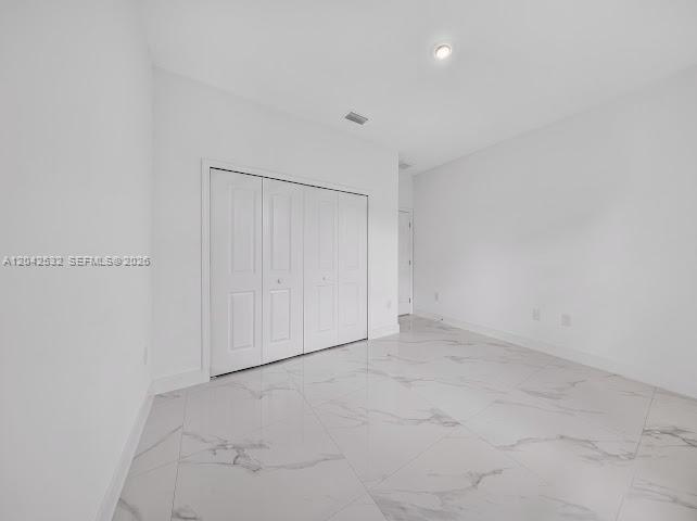 An empty bedroom features white walls, a white closet with folding doors, and marble-patterned tile flooring — 928-930 Hepburn Ave, Lehigh Acres FL 33974, LEHIGH ACRES, FL