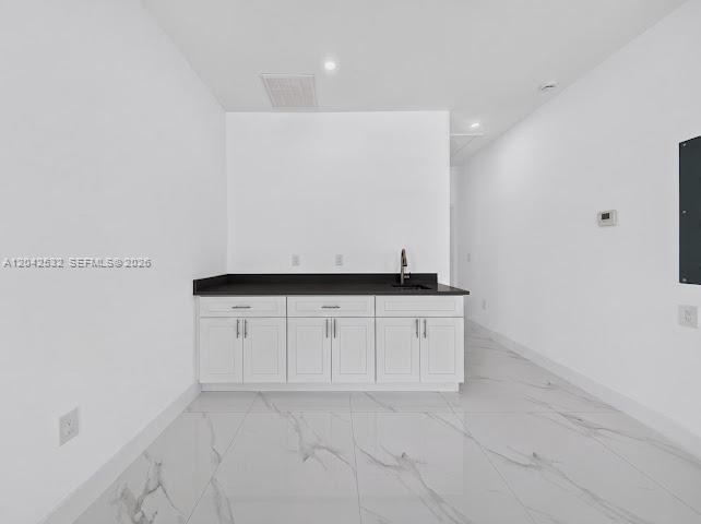 A minimalist wet bar features white cabinets, a dark countertop, and white marble-patterned tile flooring — 928-930 Hepburn Ave, Lehigh Acres FL 33974, LEHIGH ACRES, FL