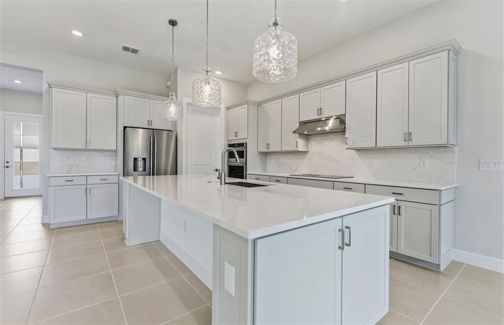 A modern kitchen features light gray cabinetry, a large white island, and stainless steel appliances — 6200 SW 82ND TERRACE ROAD, OCALA, FL