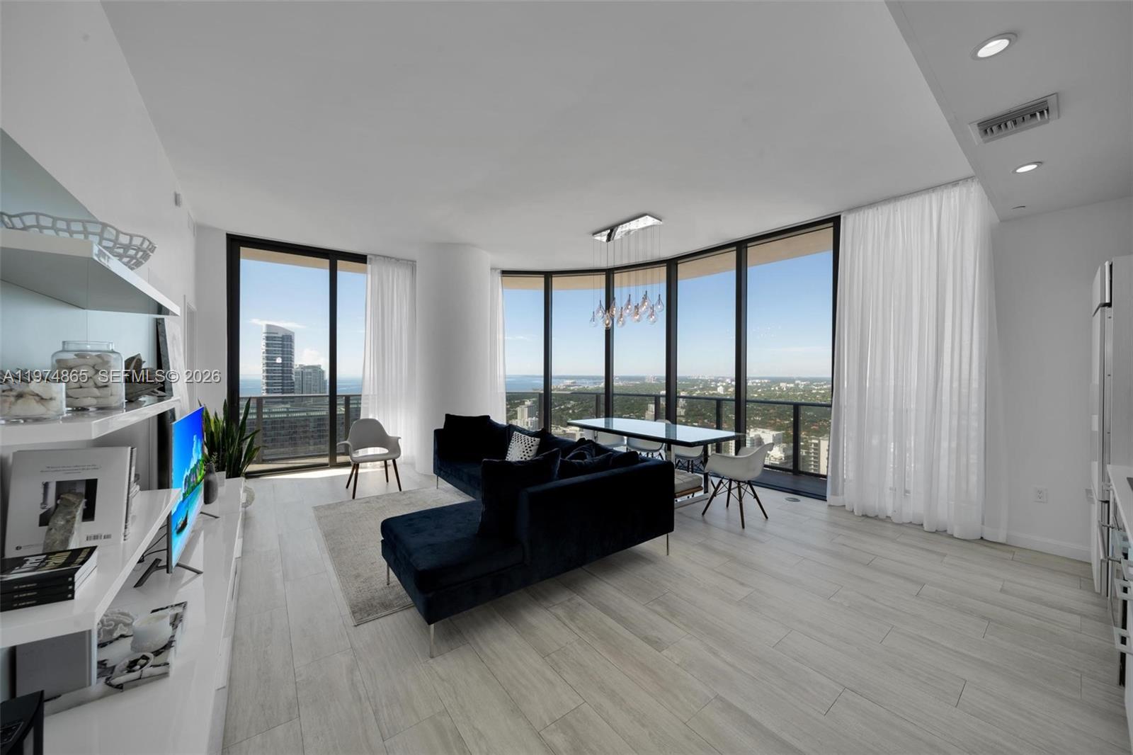 A modern living room features a dark blue sectional sofa, dining area, and floor-to-ceiling windows — 55 SW 9th St # 4406, Miami FL 33130, MIAMI, FL