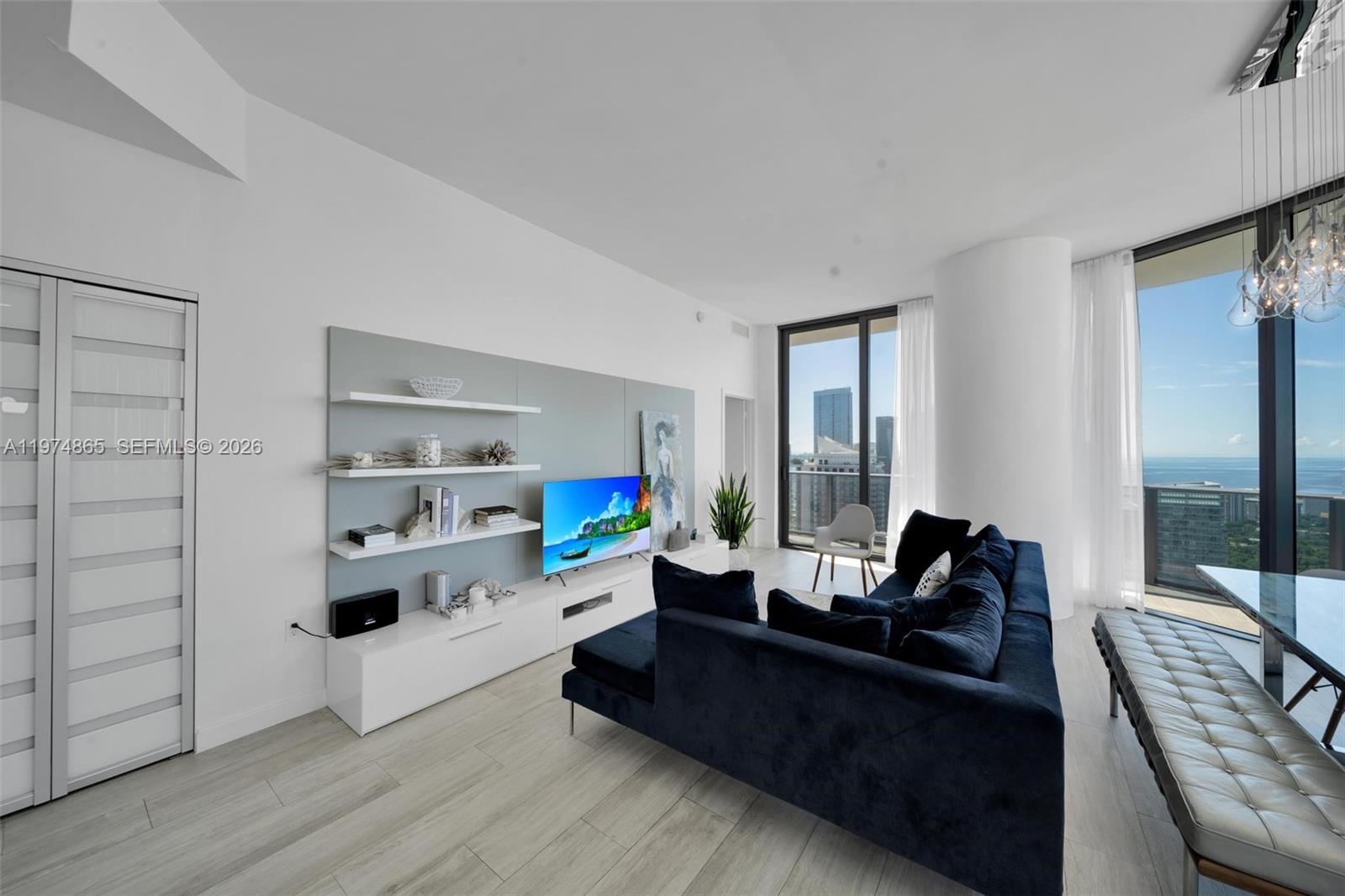 A modern living room features a navy sectional sofa, white shelving, and floor-to-ceiling windows — 55 SW 9th St # 4406, Miami FL 33130, MIAMI, FL