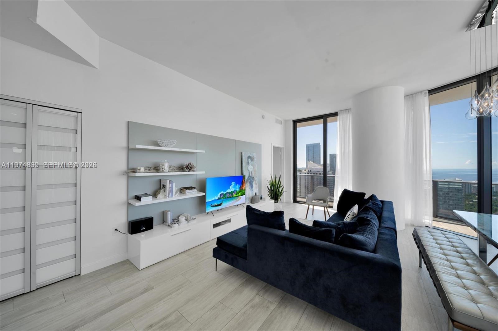 A modern living room features a blue sectional sofa, floating shelves, and floor-to-ceiling windows — 55 SW 9th St # 4406, Miami FL 33130, MIAMI, FL