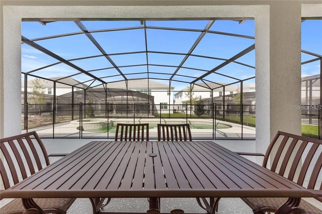 A patio table and chairs sit on a covered lanai overlooking a screened-in swimming pool — 2626 CALISTOGA AVENUE, KISSIMMEE, FL