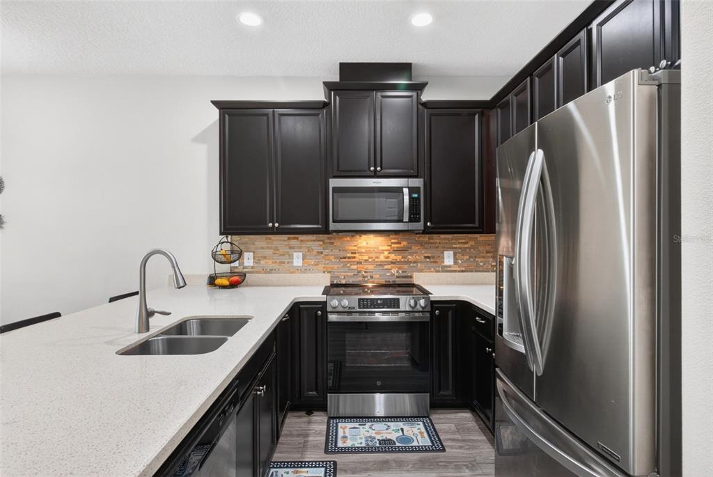 A kitchen features dark wood cabinets, stainless steel appliances, and light-colored quartz countertops — 2535 FASSONA DRIVE, KISSIMMEE, FL